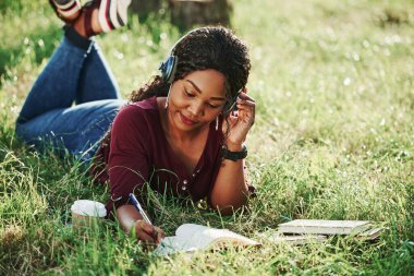 Müzik genç kadın yazarlara konsantre olmalarına yardımcı olur. Yazın parktaki neşeli Afrikalı Amerikalı kadın..