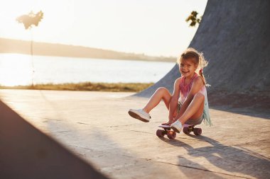 Paten kayıyor. Güneşli bir gün. Çocuk rampada iyi eğlenceler. Neşeli küçük kız.