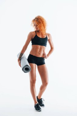 Gri renkli paspası elinde tutuyor. Kızıl saçlı kadın vücut geliştirici beyaz arka planda stüdyoda..