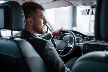 Rahat aracın tadını çıkarıyorum. Modern iş adamı yeni arabasını otomobil salonunda deniyor..