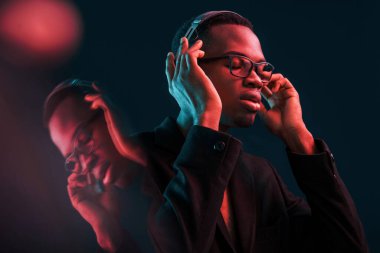 Kulaklıkla müzik dinlemeyi seviyorum. Gözlüklü. Fütürist neon ışıkları. Stüdyodaki Afrikalı Amerikalı genç adam..