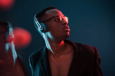 Kulaklıkla müzik dinlemeyi seviyorum. Gözlüklü. Fütürist neon ışıkları. Stüdyodaki Afrikalı Amerikalı genç adam..