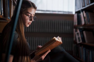 Okumaya odaklan. Kütüphanede kitaplarla dolu bir kız öğrenci var. Eğitim kavramı.