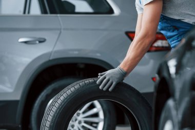 Gri gömlek. Tamirhanede lastik tutan bir tamirci. Kış ve yaz lastiklerinin değiştirilmesi.