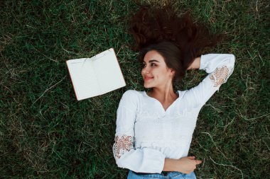 Not defteri yan tarafta. Kız yeşil çimlere uzanıp dinleniyor..