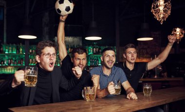 Futbol topuyla. Bu bir gol. Zaferi kutluyoruz. Üç sporsever bir barda ellerinde birayla maç izliyorlar..