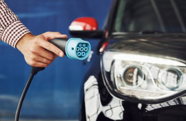 Adam elektrikli bir arabanın karşısında duruyor ve şarj halatını tutuyor..