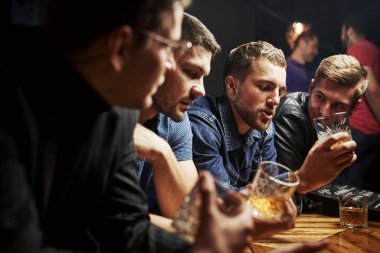 Yan görüş. Arkadaşlar ellerinde alkolle barda dinleniyorlar. Sohbet ederken.