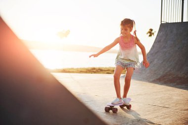 Güneşli bir gün. Çocuk rampada paten kayarken eğleniyor. Neşeli küçük kız.