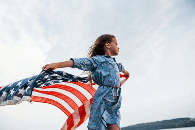 Amerikan Bayrağı elinde olan vatansever kadın çocuk. Bulutlu gökyüzüne karşı.