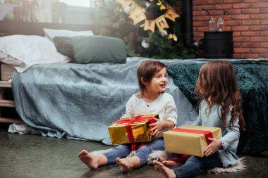 Gülümseyen çocuklar. Noel tatili ve yatağın yanındaki güzel odada oturan bu iki çocuk için hediyeler..