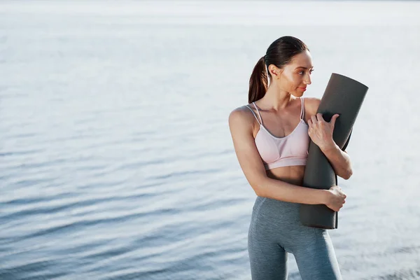 Houdt Rolmat Handen Meisje Sportieve Kleding Staat Tegen Water Achtergrond — Stockfoto