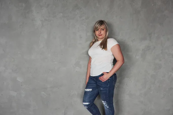 穿休闲裤工作室里的年轻白人妇女站在灰暗的背景下 — 图库照片