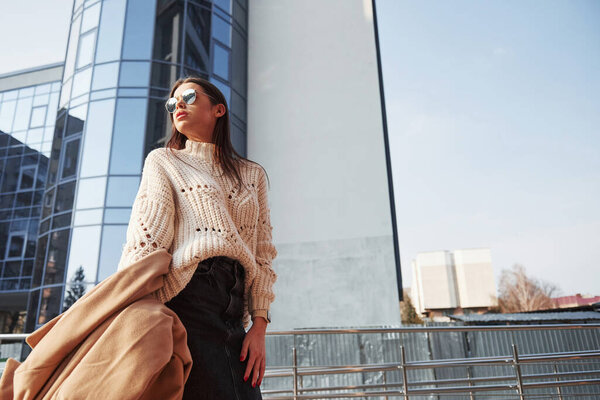 Незаконченное здание позади. Молодая красивая девушка в теплой одежде прогуливалась по городу в выходные дни.