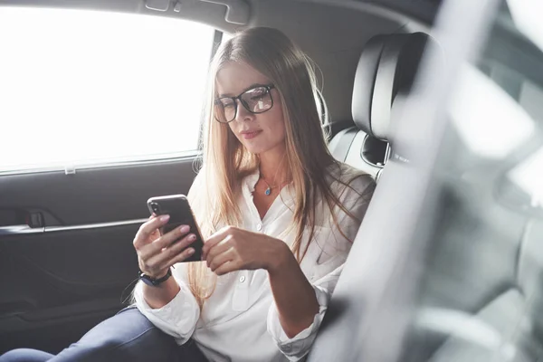 Usando Smartphone Hermosa Chica Rubia Sentada Coche Nuevo Con Interior — Foto de Stock