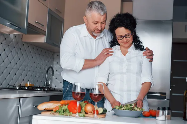 一緒に幸せだ 台所で野菜を使った料理を作る白いシャツを着た男と妻 — ストック写真