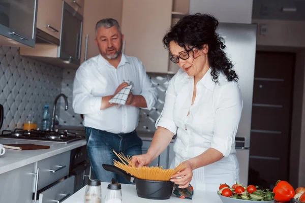 いい仕事だ 台所で野菜を使った料理を作る白いシャツを着た男と妻 — ストック写真