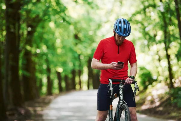 Segurando Smartphone Ciclista Uma Bicicleta Está Estrada Asfalto Floresta Dia — Fotografia de Stock
