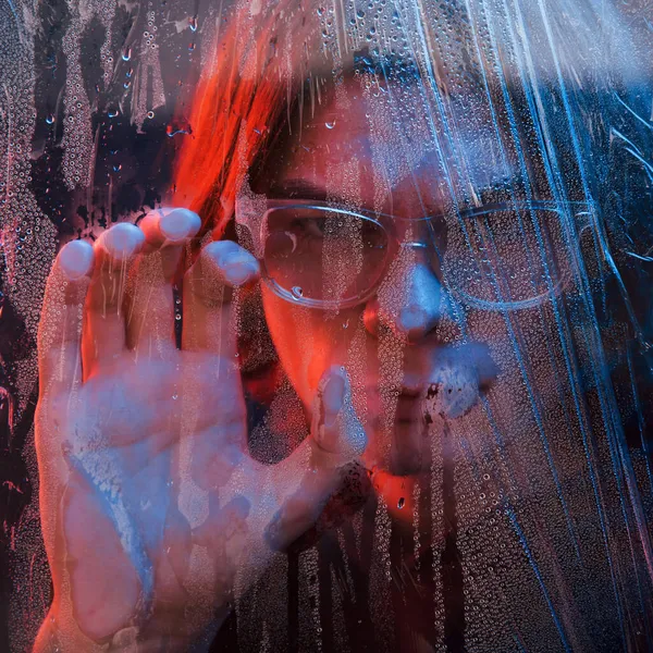正面図 スタジオはネオンで暗いスタジオで撮影しました 濡れたガラスの後ろに深刻な男の肖像画 — ストック写真