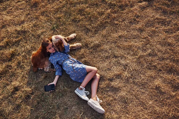 最上階だ 黒い電話で草の上に横たわる かわいい女の子持っていますA散歩とともに彼女の犬屋外で晴れた日 — ストック写真