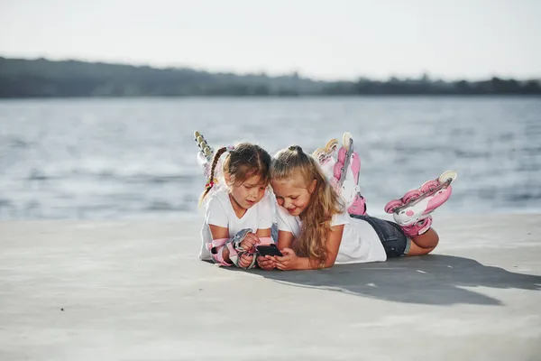 Using Smartphone Two Little Girls Roller Skates Outdoors Lake Background — Stock Photo, Image