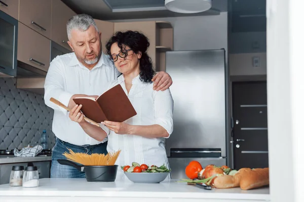 後を追う必要がある 台所で野菜を使った料理を作る白いシャツを着た男と妻 — ストック写真