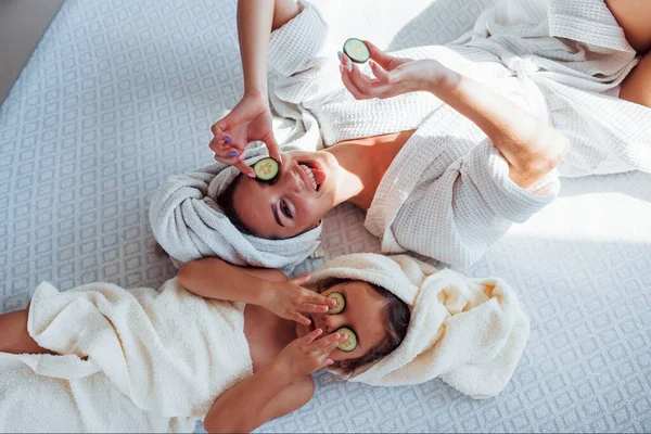 若いです正の母と娘とともにタオル頭の上に寝そべってベッドの上に一緒にキュウリ — ストック写真