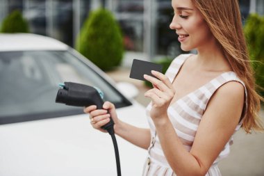 Siyah kart taşıyor. Elektrikli arabalardaki kadın gündüz şarj istasyonunda. Yepyeni bir araç..