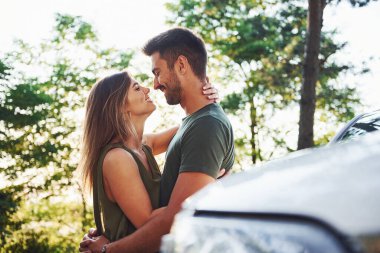 Beyaz arabanın ön tarafında. Genç ve güzel bir çift gündüz vakti ormanda iyi vakit geçirir..