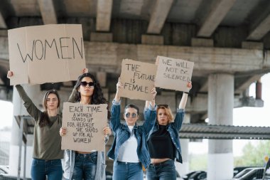 Köprünün altında duruyor. Bir grup feminist kadın dışarıda hakları için protesto yapıyor..