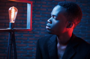 Ampule bakıyor. Fütürist neon ışıkları. Stüdyodaki Afrikalı Amerikalı genç adam..