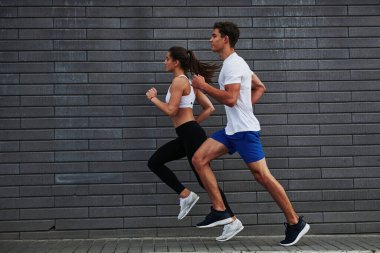 Yan görüş. Erkek ve kadının fitness günü ve şehirde gündüz vakti tuğla duvarın yanında koşuyorlar..