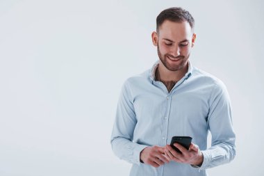 Akıllı telefon kullanarak eğleniyorum. Resmi kıyafetli adam stüdyoda beyaz arka plana karşı duruyor..