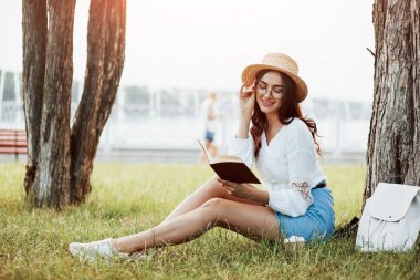 Kitapla rahatlayan hoş bir kız. Genç bir kadın hafta sonu geçirir ve gündüz vakti parkta oturur..