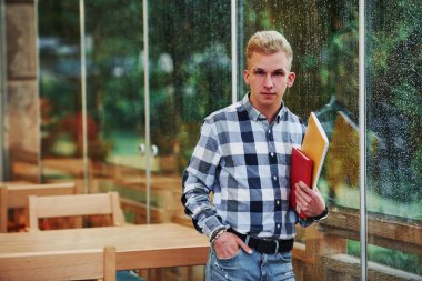 Not defterlerini elinde tutuyor. Yağmurlu bir günde kafede duran genç bir öğrencinin portresi. Bir kişi..