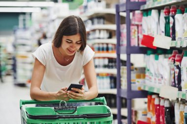 Akıllı telefon kullanıyor. Piyasada günlük giysiler içinde kadın alışverişçi ürün arıyor..