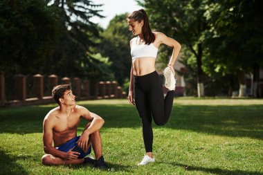 Elinde akıllı telefonla oturan ve dinlenen adam. Erkek ve kadının şehirde gündüz vakti parkta fitness günü var..