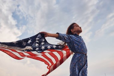 Amerikan Bayrağı elinde olan vatansever kadın çocuk. Bulutlu gökyüzüne karşı.