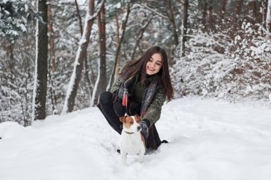 Köpeği okşamak. Kış parkında köpeğiyle yürürken gülümseyen esmer..