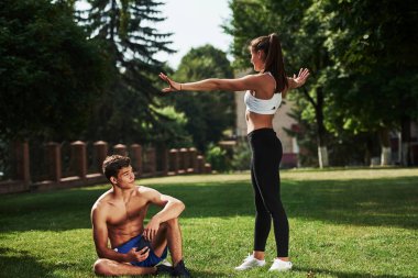 Elinde akıllı telefonla oturan ve dinlenen adam. Erkek ve kadının şehirde gündüz vakti parkta fitness günü var..