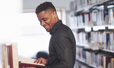 Samimi bir gülümseme. Kütüphanede kitaplarda bazı bilgiler arayan Afrikalı Amerikalı bir adam var..