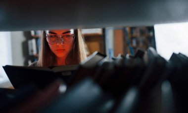 Kitaptaki yapay kırmızı ışık yanıyor. Kütüphanede kitaplarla dolu bir kız öğrenci var. Eğitim kavramı.