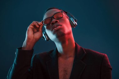 Kulaklıkla müzik dinlemeyi seviyorum. Gözlüklü. Fütürist neon ışıkları. Stüdyodaki Afrikalı Amerikalı genç adam..