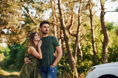 Beyaz renkli arabanın yanında. Genç ve güzel bir çift gündüz vakti ormanda iyi vakit geçirir..