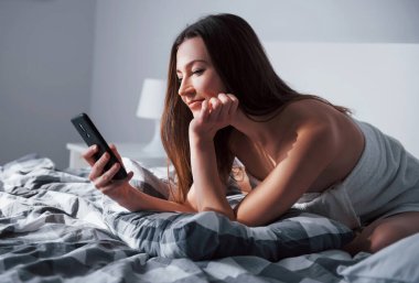 Sosyal medyayı kullanarak. Güzel genç bir kadın, sabahları yatağında uzanıyor..