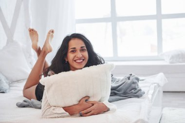 Karnının üstüne yatıp gülümsüyor. Esmer, gündüz vakti yatak odasındaki beyaz kanepede dinleniyor..