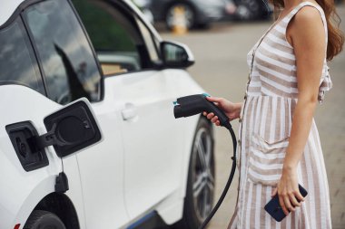 Elektrikli arabalardaki kadın gündüz şarj istasyonunda. Yepyeni bir araç..