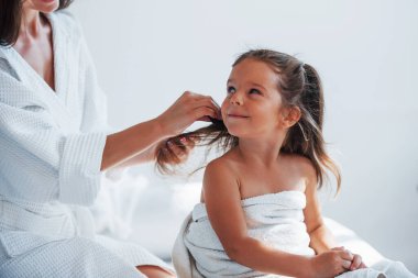 Saç modeline yardım ediyorum. Genç anne kızıyla birlikte beyaz odada güzel bir gün geçiriyor..