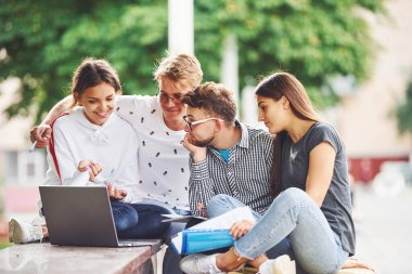 İşine odaklan. Dizüstü bilgisayarla. Gündüz vakti şehirde günlük kıyafetler giyen bir grup genç öğrenci..
