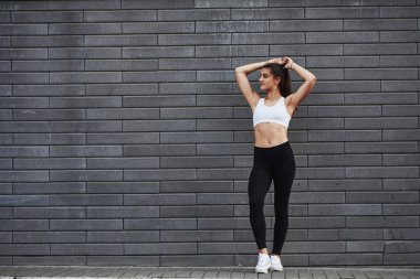 Genç, sportif esmer, ince vücutlu, şehirde gündüz vakti tuğla duvara yaslanmış..
